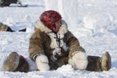 Inuit toddler sits in the snow and watches at Hamlet Day. Igloolik. Nunavut. Canada. 2008