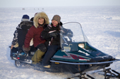 Inuit girl Sarah Jane Qulaut drives her mother Renee and friends on a snowmobile. Igloolik. Nunavut, Canada. 2008
