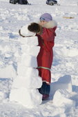 Kaja Natar, an Inuit girl from Igloolik wearing a traditional parka, piles up bricks of snow while. Nunavut, Canada. 2008
