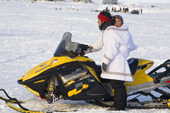 Bernadette Arnatsiaq, an Inuit woman, gets onto her snowmobile wearing a traditional Baffin Island parka with he baby in the hood. Igloolik, Nunavut, Canada. 2008