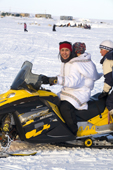 Bernadette Arnatsiaq, an Inuit woman, gets onto her snowmobile wearing a traditional Baffin Island parka with her baby in the hood. Igloolik, Nunavut, Canada. 2008