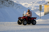 Carrying a baby in her Amautiq, a young Inuit woman drives a 4 wheeler along a street in Pangnirtung. Nunavut, Canada. 2008