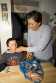 While cleaning Arctic Char, Alukie, an Inuit woman from Pangnirtung feeds a fish eye to her son Aidan. Nunavut, Canada. 2008