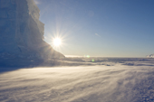 Sun flare through wind drift across sea ice close to an iceberg. Luitpold Coast East Antarctica