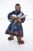 Wearing traditional reindeer skin Malitsa (tunic) & boots, Edik Serotetto, a young Nenets man, carrying Muksun he has caught in a net set under the sea ice. Seyakha, Yamal Peninsula, Western Siberia, Russia