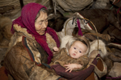 Nyaka, an elderly Nenets woman, holds her grandaughter in a cradle inside their reindeer skin tent.Tambey tundra, Yamal Peninsula, Western Siberia, Russia.