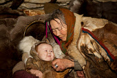 Nyaka, an elderly Nenets woman, takes care of her grandaughter in a cradle inside their reindeer skin tent.Tambey tundra, Yamal Peninsula, Northwest Siberia, Russia.