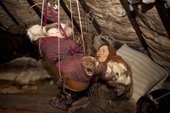 Nyaka, an elderly Nenets woman, rocks her grandaughter in a cradle inside their reindeer skin tent.Tambey tundra, Yamal Peninsula, Western Siberia, Russia.