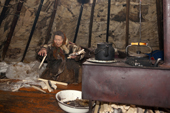 Nyaka, an elderly Nenets woman, tends the stove inside her family's reindeer skin tent.Tambey tundra, Yamal Peninsula, Western Siberia, Russia.