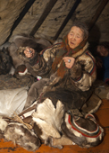 Nyaka, an elderly Nenets woman, using reindeer sinew to sew traditional clothing inside her family's reindeer skin tent. Tambey tundra, Yamal Peninsula, Western Siberia, Russia.