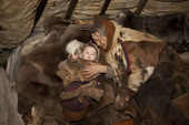 Nyaka, an elderly Nenets woman, comforts her baby grandaughter in a cradle inside their reindeer skin tent. Tambey tundra, Yamal Peninsula, Western Siberia, Russia.