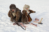 At their winter camp,Emma Vanuito, a Nenets woman, saws up frozen reindeer meat, with her daughter, Nenya, close by. Tambey. Yamal Peninsula, Western Siberia, Russia.