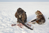 At their winter camp, Emma Vanuito, a Nenets woman, saws up frozen reindeer meat, with her daughter, Nenya, close by. Tambey. Yamal Peninsula, Western Siberia, Russia.