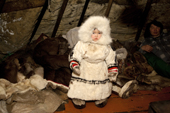 Nenya Vanuito, a two year old Nenets girl, dressed in traditional warm reindeer skin clothing, before going to play outside in the cold. Tambey. Yamal Peninsula, Western Siberia, Russia.