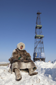 Jakov Vanuito, a Nenets reindeer herder, sits in front of a gas drilling derrick near Tambey in the South Tambey gas field. Yamal Peninsula, Western Siberia, Russia
