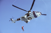 Crew member of a rescue helicopter is winched down onto a boat to rescue an injured sailor. Spitsbergen.